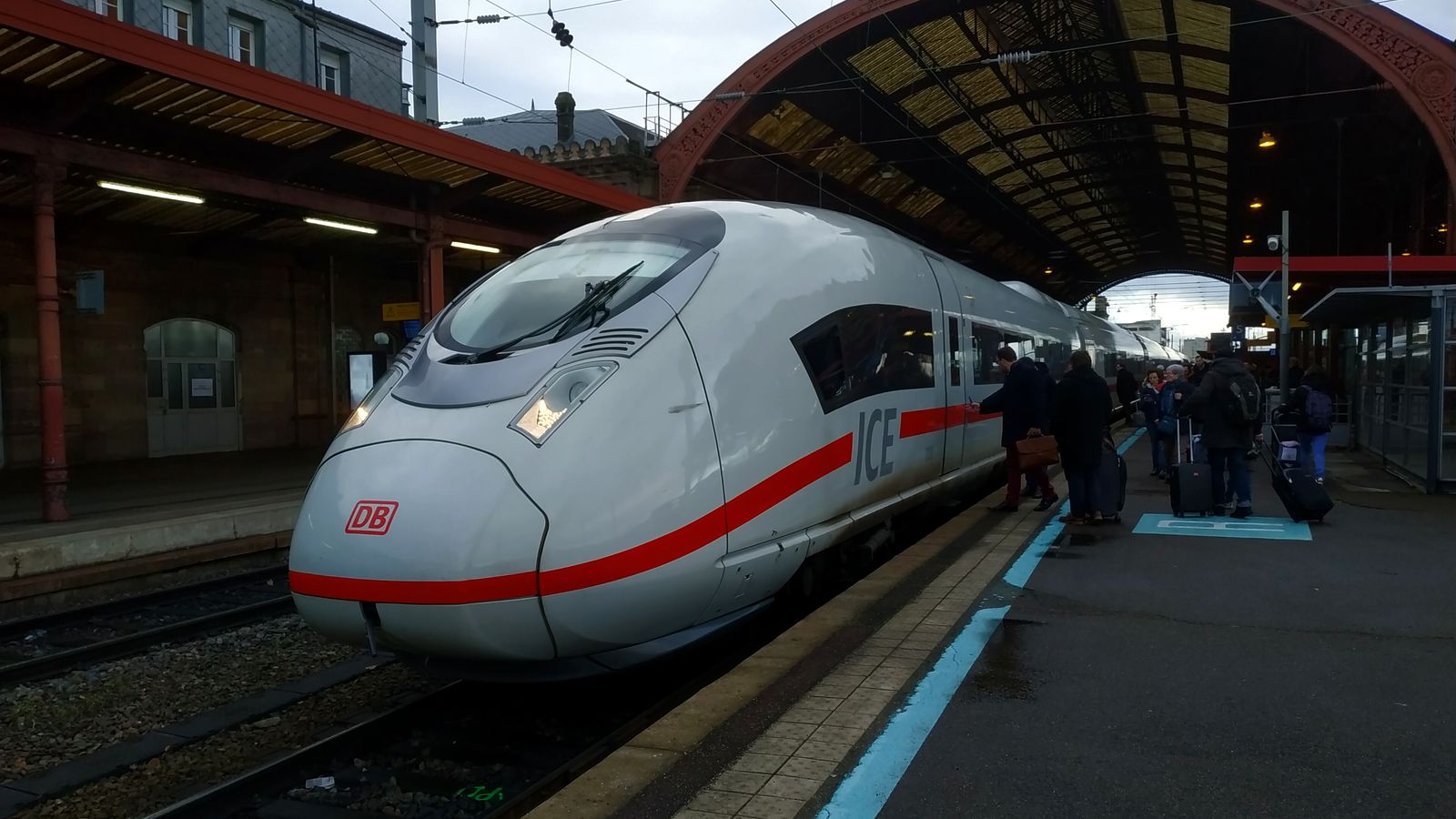 ICE 3 der Baureihe 407 am Bahnsteig im Bahnhof Strasbourg, dahinter die rote Bogenhalle aus Stahl und Glas, Reisende mit Koffern steigen ein
