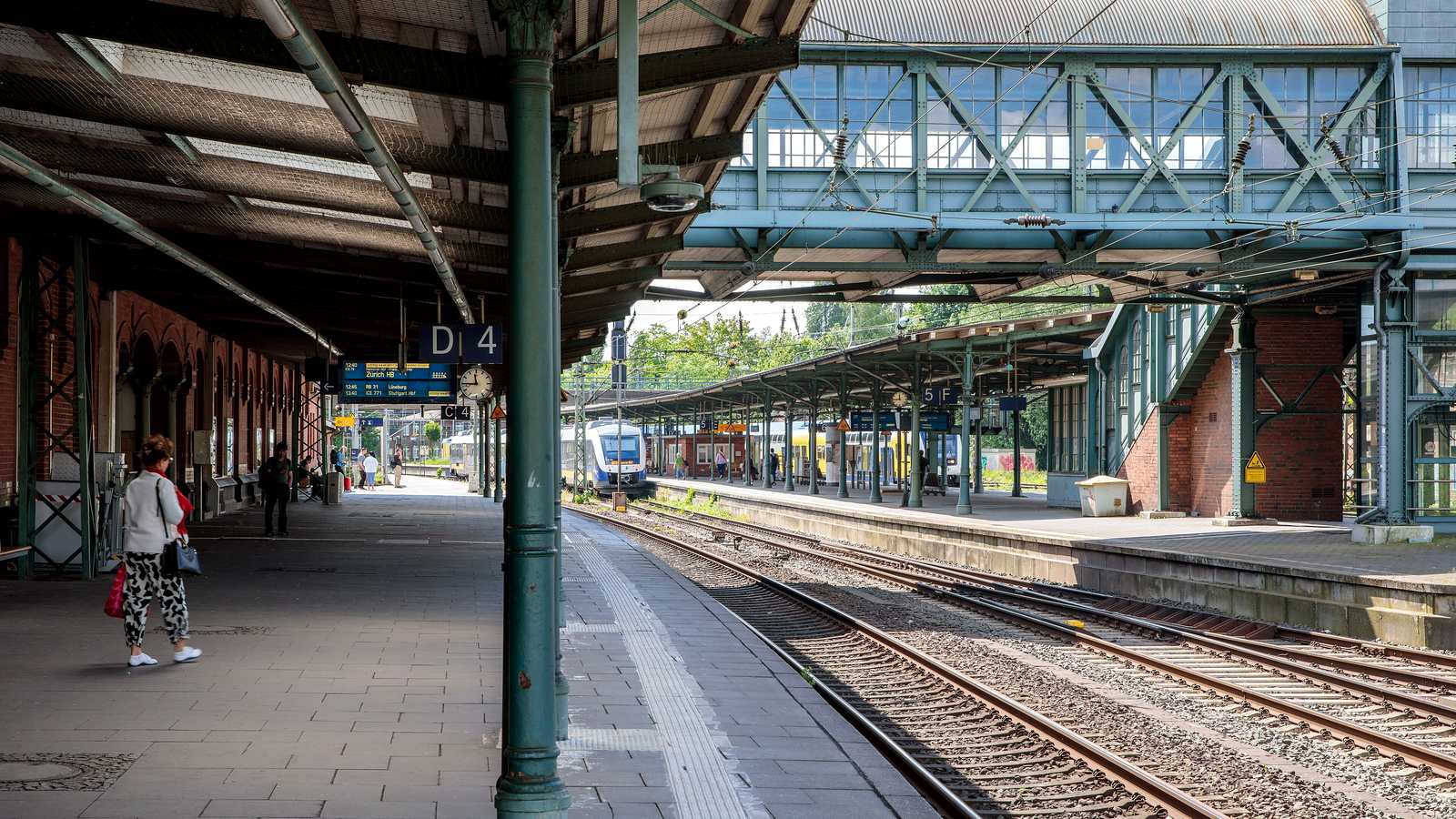 Überdachte Bahnsteige des Bahnhofs Hamburg-Harburg mit grünen Stahlstützen, Abschnittsschild D 4 und einer verglasten Fußgängerbrücke über den Gleisen, im Hintergrund ein Regionalzug